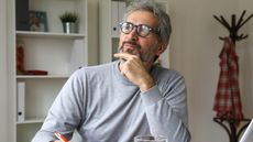 A man looks thoughtful while sitting at his desk in his home office.