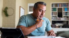 An older man concentrates as he looks over paperwork and uses a calculator.