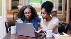 An older woman and her daughter look at a laptop together, looking serious.