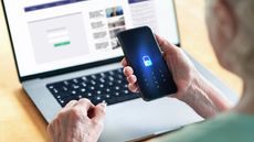 A man holds a locked phone in front of a computer.