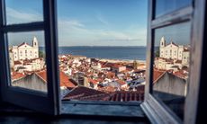 View of tile roofs and the sea from a hotel room in Europe.