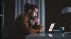 A man studies his laptop at his kitchen table.