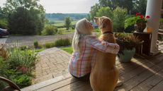 A woman sits on her front porch with her dog.