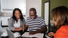 A couple smile as they work on paperwork at a desk, across from a financial adviser.