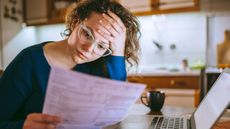 Woman wearing glasses reading over paperwork while sitting in front of a computer.