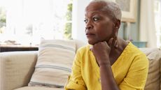 An older woman sitting on her sofa looks worried. 