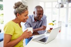 A mature couple using a laptop at breakfast.